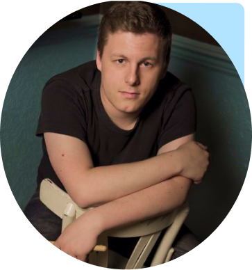 Josh sitting on a backwards chair holding drumsticks